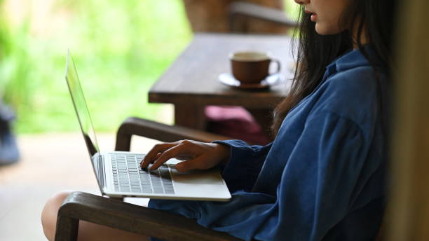 istock Close-up woman is using a computer laptop while sitting at the wooden chair. 1248763824