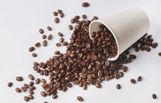 Studio shot of a tipped over paper cup filled with coffee beans against a white background