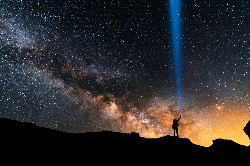 Beautiful starry sky with bright milky way galaxy. Night landscape . Person silhouette with flashlight illuminate starry sky.
