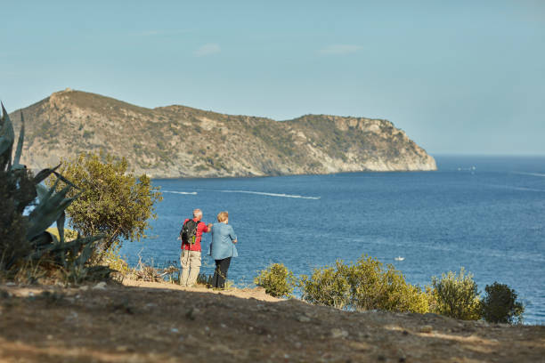 Senior couple in their 70s standing at vista point on coastal trail and enjoying view of Mediterranean Sea.
