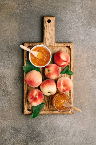 pfirsich marmelade oder marmelade in glas und schüssel auf holzschneidebrett. essen hintergrund, top-ansicht - can fruit peaches healthy eating stock-fotos und bilder