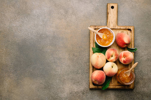 confiture de pêche ou marmelade dans un bocal en verre et bol sur planche à découper en bois. fond de nourriture, vue supérieure - preserves jar apricot marmalade photos et images de collection