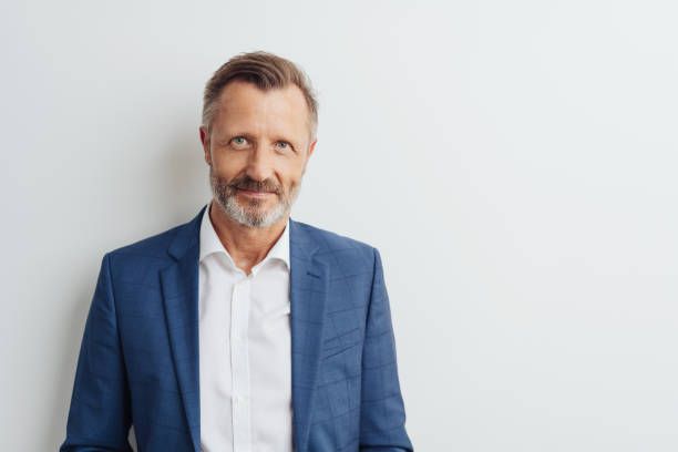 Middle-aged man in blue blazer, copy space Handsome and friendly middle-aged bearded man in white shirt and unbuttoned blue blazer front half length portrait against white wall with copy space looking at camera photos stock pictures, royalty-free photos & images