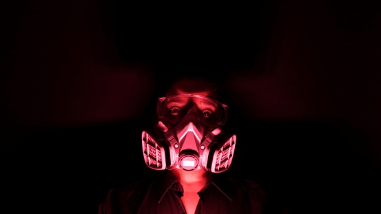 Woman in biohazard medical mask in blackness with red glow light. Home quarantine isolation from Coronavirus or covid-19. Apocalyptic, depression mood of global flu epidemic and virus protection concept.