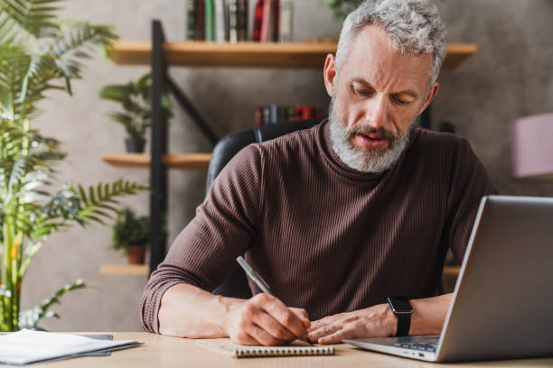 istock Middle aged businessman in casual clothes making notes in notepad while sitting in his office 1248775609
