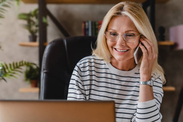 istock Smiling casual senior woman using laptop while talking on smartphone. 1248775687