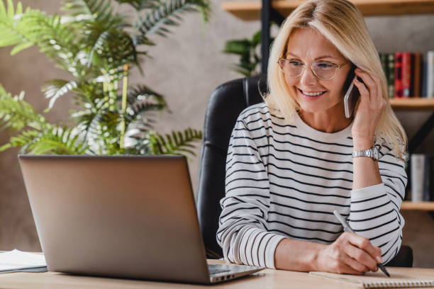 istock Beautiful elderly businesswoman speaking on smart phone while working and writing notes in notepad 1248775703