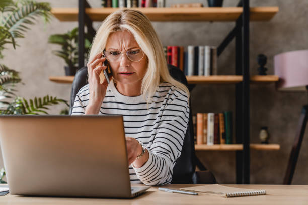 istock Mature woman looking stressed while using laptop and talking on mobile phone 1248775736