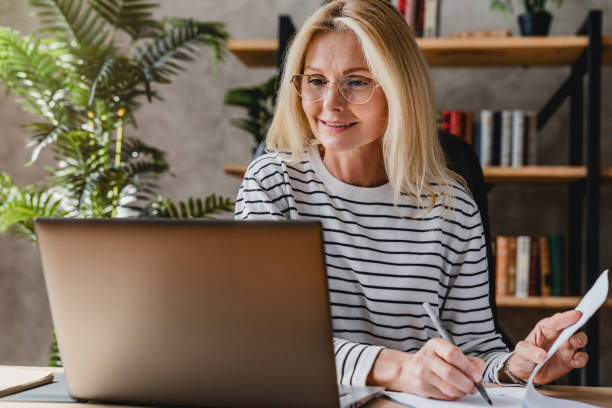 istock Senior stylish woman taking notes in notebook while using laptop at home office 1248775767