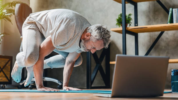 homem em bakasana pose fazendo vinyasa yoga fluxo em casa. praticando yoga em casa - parada de mãos - fotografias e filmes do acervo