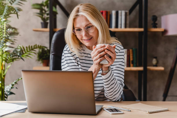 istock Portrait of happy senior woman using laptop while drinking coffee at workplace 1248775879