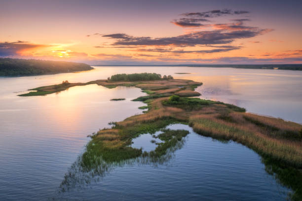 aerial view of beautiful small islands with green trees and grass on the river at sunset in summer. colorful landscape with island, meadows, orange sky reflection in blue water. top view. nature - coastline aerial view forest pond imagens e fotografias de stock