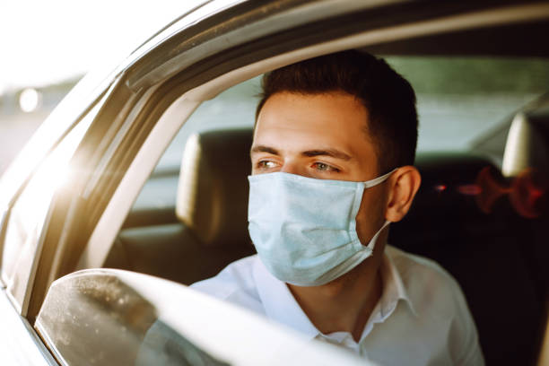 man driving a car puts on a medical mask during an epidemic in quarantine city. - illness mask pollution car imagens e fotografias de stock