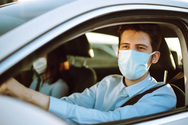 el hombre que conduce un coche se pone una máscara médica durante una epidemia en la ciudad de cuarentena. - personal land vehicle fotos fotografías e imágenes de stock
