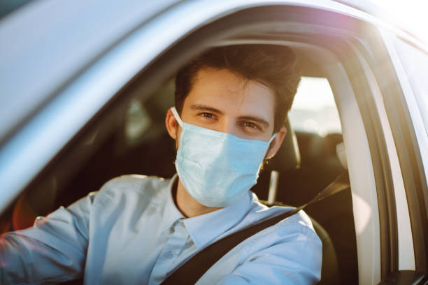 man driving a car puts on a medical mask during an epidemic in quarantine city. - illness mask pollution car imagens e fotografias de stock