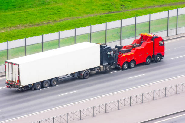 leistungsstarke große rig sattelzug traktor schleppt mit befestigten defekten evakuierten lkw mit containeranhänger fahren auf der stadtautobahn, luftbild. - towing tow truck truck semi truck stock-fotos und bilder