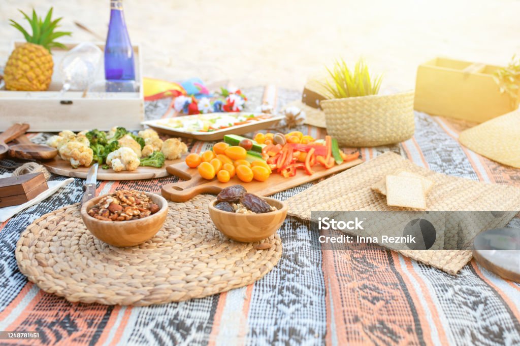 Beautiful summer picnic on the beach at sunset in zero waste style. Eco friendly idea for weekend staycations Beautiful summer picnic on the beach at sunset in zero waste style. Organic fresh fruit, cheese and vegetables on linen blanket. Eco friendly idea for weekend staycations. Picnic Stock Photo