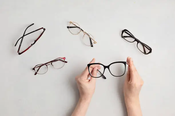 Photo of Woman hand holding eyeglasses. Optical store, glasses selection, eye test, vision examination at optician, fashion accessories concept. Top view