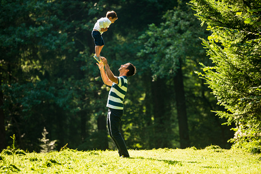 Happy family plays outdoors at a clearing. The father holds his little son up in the air.