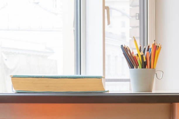 istock Old thick book and plastic gray cup with pencils on desk at window. Copy space for text. 1248786838