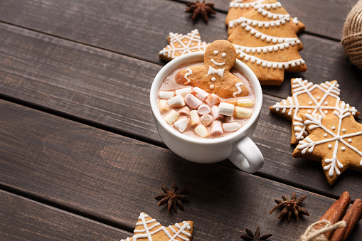 Christmas time. Gingerbread man in cup of cocoa with marshmallows and sweets on wooden table, copy space