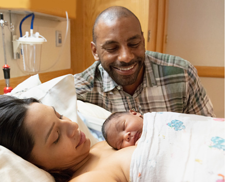 Mixed race family admiring their newborn baby at hospital with mother