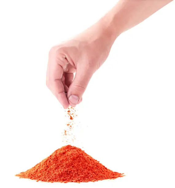 A pile of red pepper is poured by a hand closeup on a white background. Isolated
