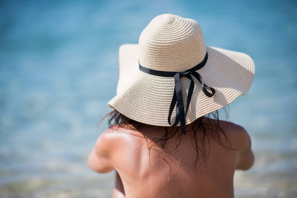 Travel. Contemplating the sea. Portrait of woman with straw hat sitting by the sea.