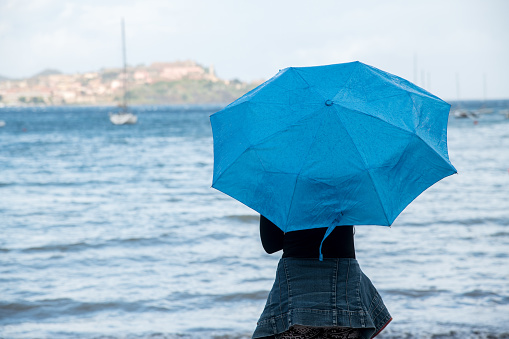 Woman with blue umbrella observing the sea on a rainy day.