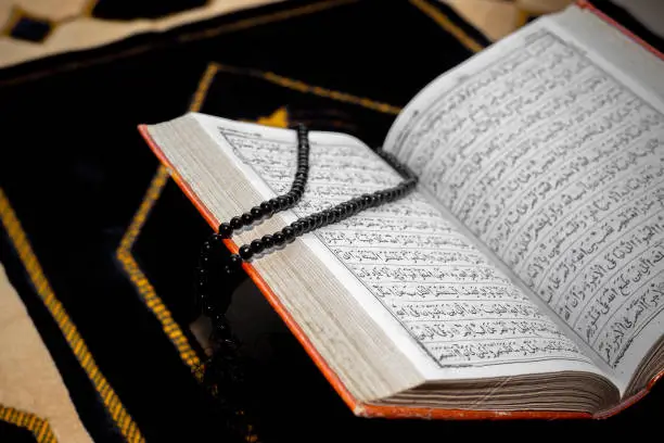 An open The holy Quran with black Tasbeeh. The Holy Quran on the mat of prayers. Focus on font and pages.