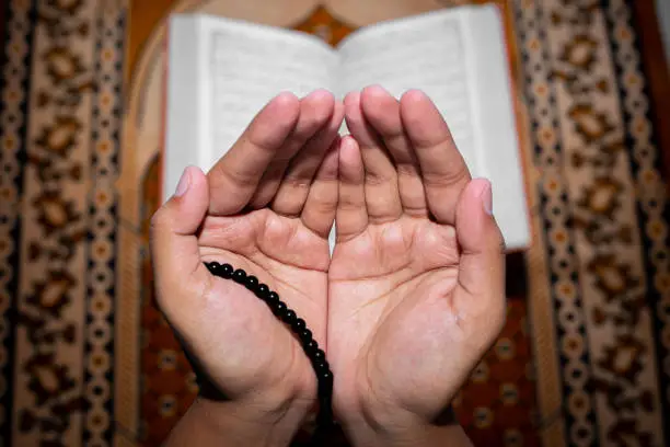 Young Muslim woman praying with Tasbeeh. The Holy Quran is the background, Indoors. Focus on hands.