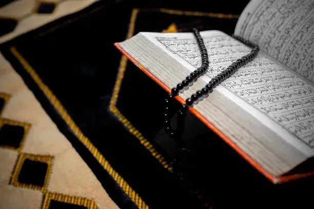 An open The holy Quran with black Tasbeeh. The Holy Quran on the mat of prayers. Focus on font and pages.
