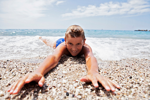 Boy laying on the shore, letting waves cover him