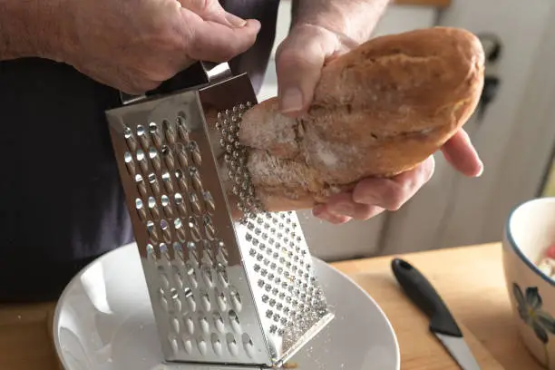 Hands of a man are grating hard bread on a grater to get breadcrumbs, selected focus, little motion blur