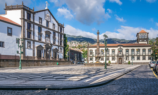 Funchal, Portugal -  November 10, 2019: Praca do Municipio, the Town Hall with its impressive doorway carved in grey stone, a fountain showing an obelisk and Church of Saint John the Evangelist of the College of Funchal, Madeira