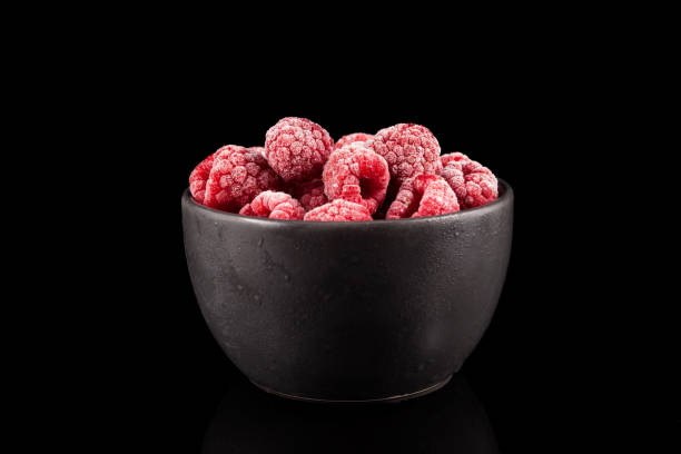Frozen raspberries in a dark bowl on a black background. Closeup. Copy space