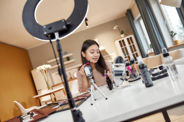 istock Makeup Artist. Asian female blogger applying makeup while recording a tutorial video for her beauty blog using camera at home 1248811351