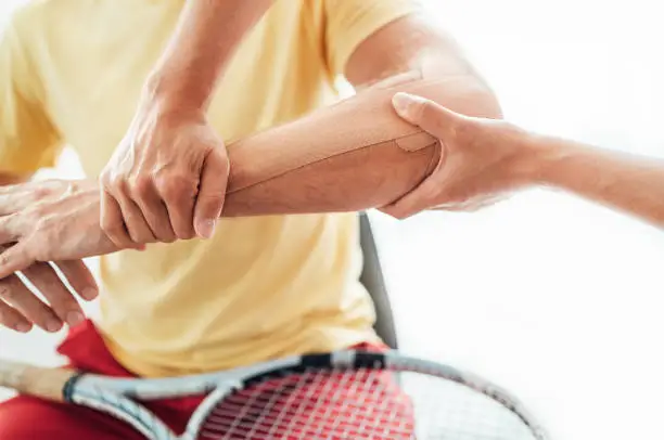 Photo of Tennis player elbow taped with elastic therapeutic or Kinesio tape applied by nurse at orthopedic ward close up image. Active sporty people health rehabilitation concept image.