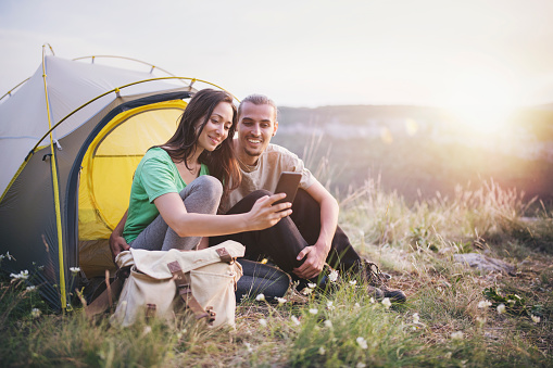 Young couple on camping in the mountain , they using smart phone and smiling.