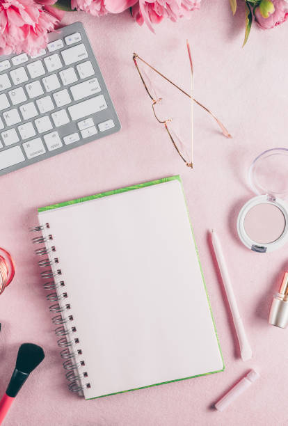 istock Office feminine desk workspace with pink peony, keyboard, cosmetics, glasses, lipstick, empty notebook on white background. 1248828373