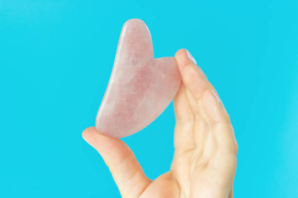 istock Pink quart guasha in a woman's hand on blue background a copy space 1248835658