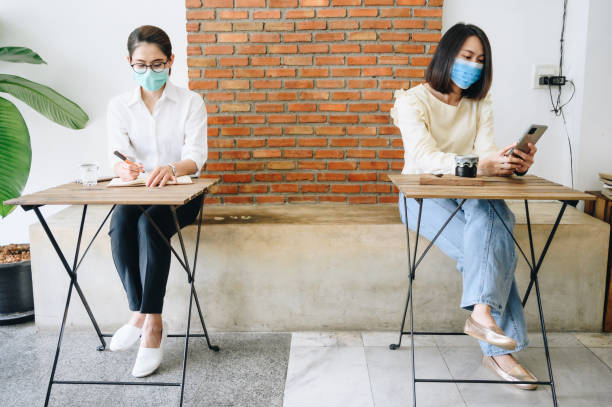 istock Two Asian woman sitting by keep space while wearing mask and do social distancing. 1248854076