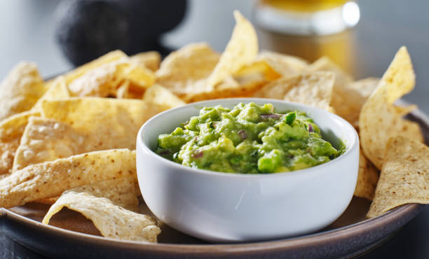 plate of corn tortilla chips with guacamole dip plate of corn tortilla chips with guacamole dip close up guacamole stock pictures, royalty-free photos & images