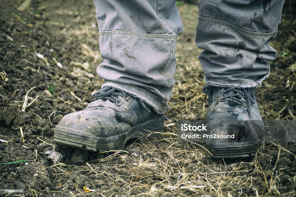 Worker's feet in dusty boots. Work clothes Worker's feet in dusty boots. A man in overalls and work boots. Work clothes Work Boot Stock Photo