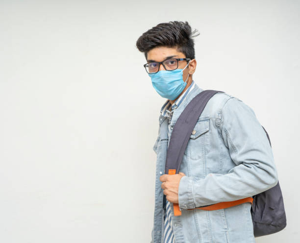 istock Young handsome asian boy ready for his college,wearing a mask, bag on his back, looking into the camera. 1248863664