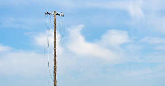 defective power pole with cut off cables in front of a blue sky with sufficient text clearance