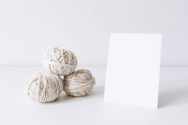 Vertical postcard mockup with white yarn on a white table background. Threads of cord wool boho image. Space for text. Good for macrame and handicrafts banners and advertisement. Copyspace mock up stock photo