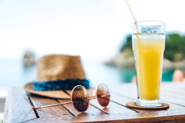 Hat, sunglasses and juice on table at seaside.