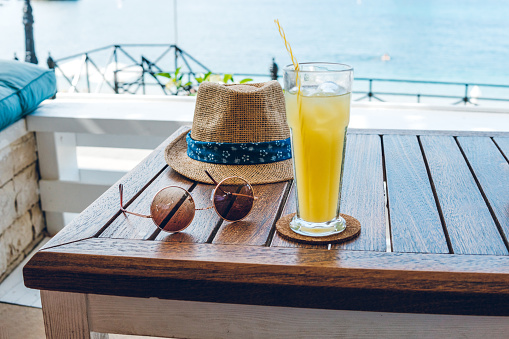 Hat, sunglasses and juice on table at seaside.