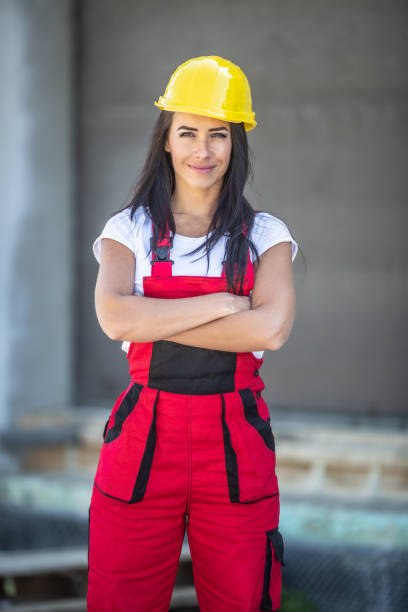 istock Female builder stands with arms crossed on a construction site dressed in work overalls and a yellow hard hat. 1248867389